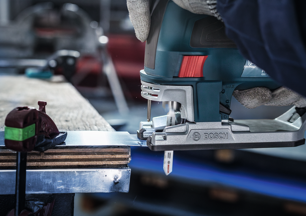 Orang yang mengenakan peralatan keselamatan memotong lembaran logam dengan gergaji ukir.