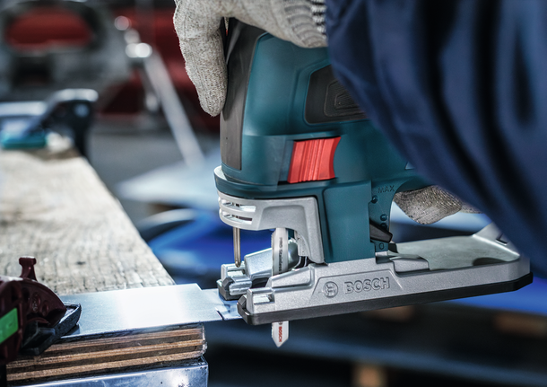 Seseorang yang mengenakan perlengkapan keselamatan menggunakan gergaji ukir untuk memotong lembaran logam.