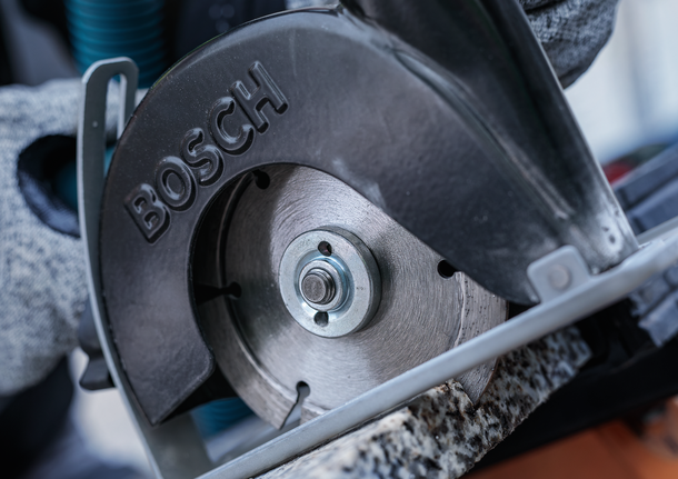 Orang yang mengenakan peralatan keselamatan memotong batu dengan gergaji bundar.