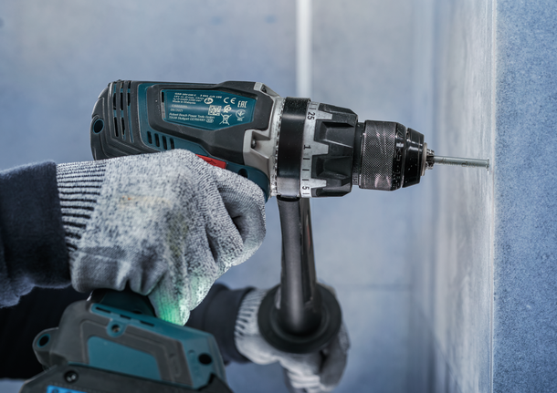 Orang yang mengenakan peralatan keselamatan mengebor sekrup ke dinding.