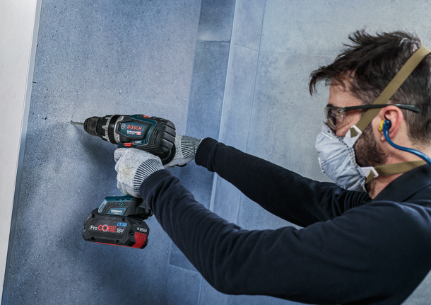 Orang yang mengenakan peralatan keselamatan mengebor tembok.
