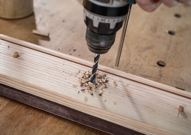 Seseorang mengebor lubang pada papan kayu di meja kerja.