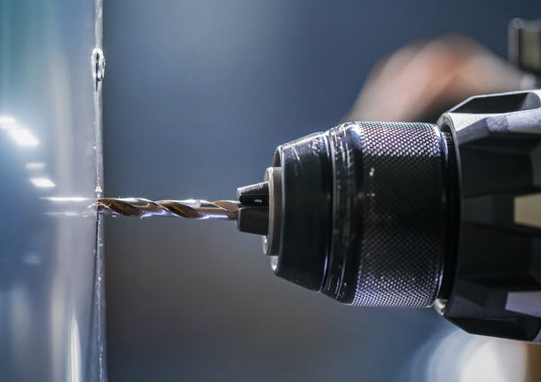 Tampilan dekat bor listrik yang membuat lubang di permukaan logam.