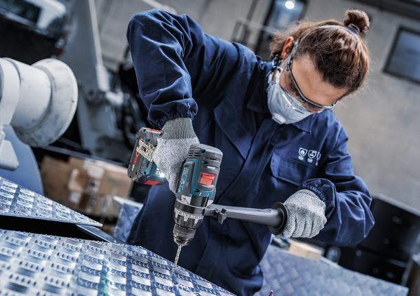 Orang yang mengenakan peralatan keselamatan mengebor pelat logam.