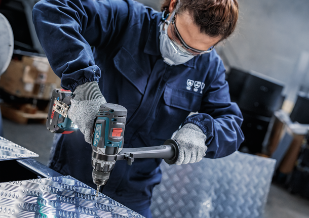 Orang yang mengenakan peralatan keselamatan mengebor lembaran logam.