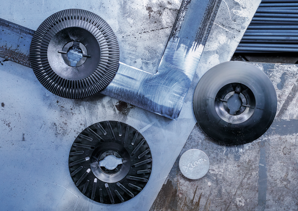 Tiga cakram penggiling dan adaptor logam tergeletak di permukaan logam yang tergores.