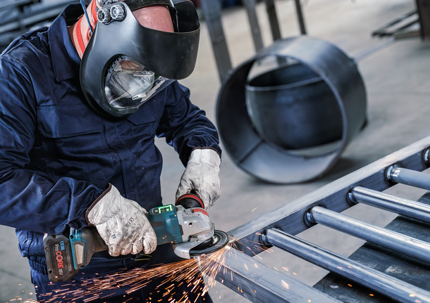 Orang yang mengenakan peralatan keselamatan menggiling logam, sehingga menimbulkan percikan api.