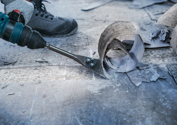 Orang yang mengenakan perlengkapan keselamatan menggunakan alat listrik untuk menyingkirkan material lantai.