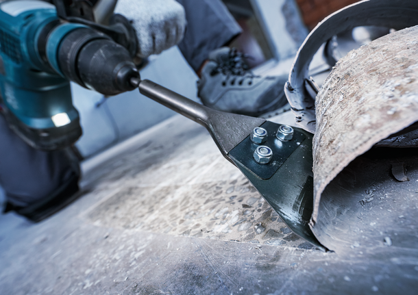 Orang yang mengenakan perlengkapan keselamatan menggunakan alat listrik untuk menyingkirkan material lantai.