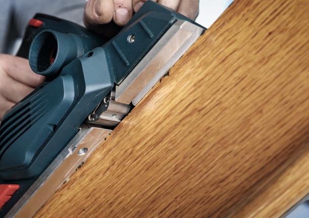 Seseorang menggunakan alat serut listrik untuk menghaluskan tepi papan kayu.