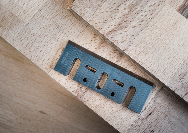 Pisau serbaguna berbahan logam diletakkan pada papan kayu bertumpuk.