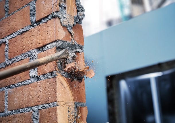 Pahat memecahkan dinding bata, menyebabkan serpihan berhamburan.