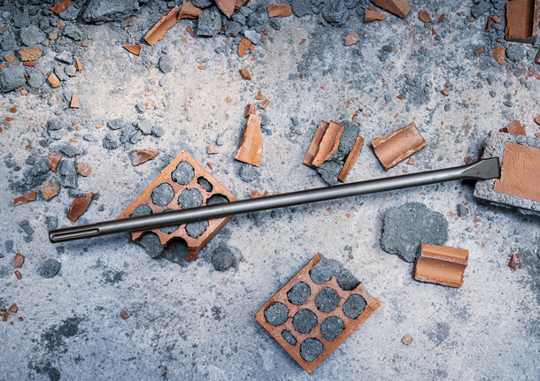 Mata pahat tergeletak di atas pecahan bata dan puing beton.