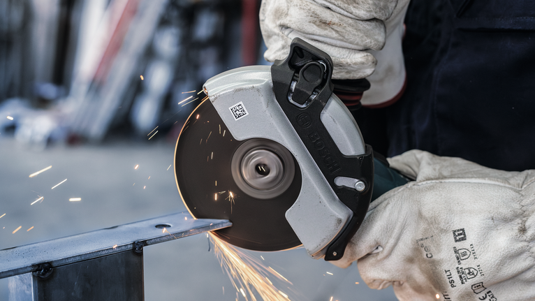 Orang yang mengenakan peralatan keselamatan memotong logam dengan penggiling sudut, menghasilkan percikan api.