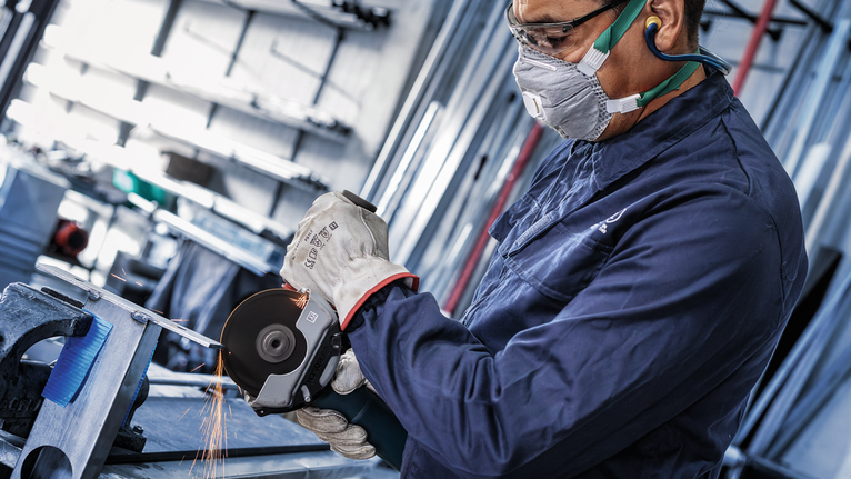 Seseorang yang mengenakan peralatan keselamatan menggiling logam, sehingga menimbulkan percikan api.