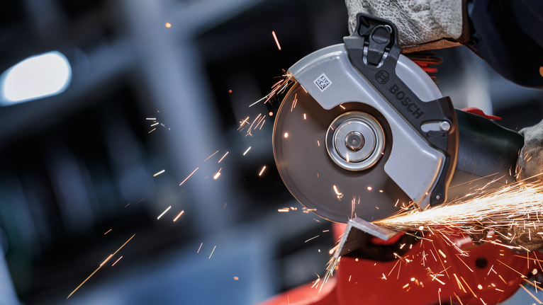 Seseorang yang mengenakan peralatan keselamatan menggiling logam, menghasilkan percikan terang.