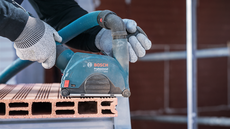 Orang yang mengenakan peralatan keselamatan mengampelas balok bata dengan perkakas listrik.