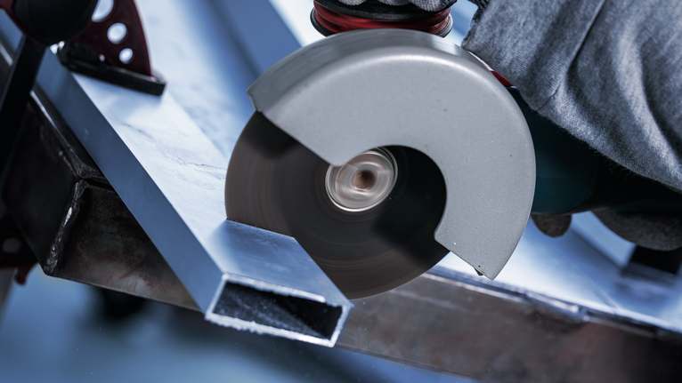 Orang yang mengenakan peralatan keselamatan memotong balok logam dengan penggiling sudut.