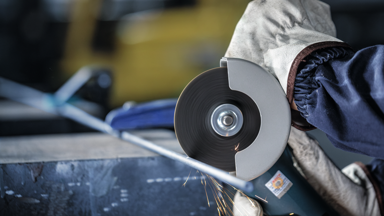 Orang yang mengenakan peralatan keselamatan memotong pipa logam menggunakan penggiling sudut.