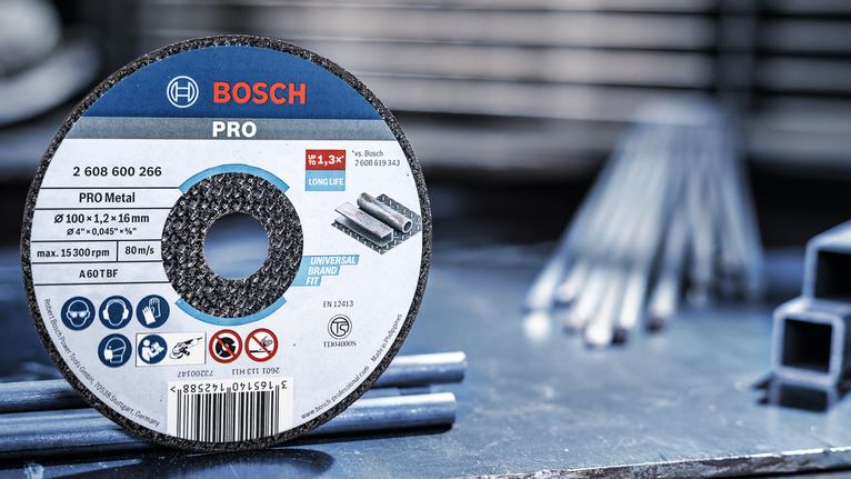 Cakram pemotong logam pada meja kerja di samping batang baja di bengkel.