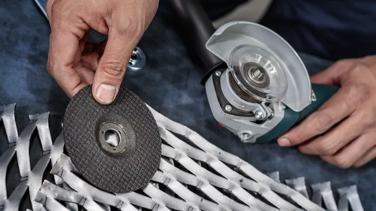 Pekerja sedang mengganti cakram penggiling pada perkakas listrik di dekat jeruji logam.