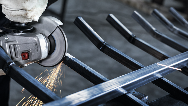 Orang yang mengenakan peralatan keselamatan menggunakan penggiling sudut untuk memotong logam, yang menimbulkan percikan api.