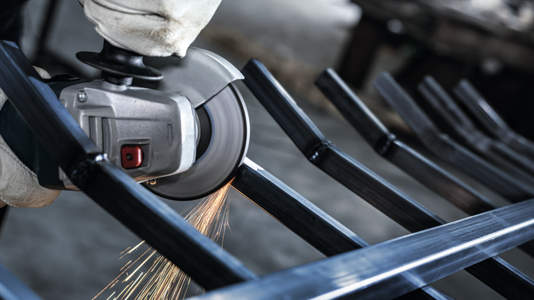 Orang yang mengenakan peralatan keselamatan menggiling batang logam, sehingga menimbulkan percikan api.