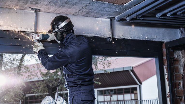 Orang yang mengenakan peralatan keselamatan menggiling balok logam, sehingga menimbulkan percikan api di dalam ruangan.