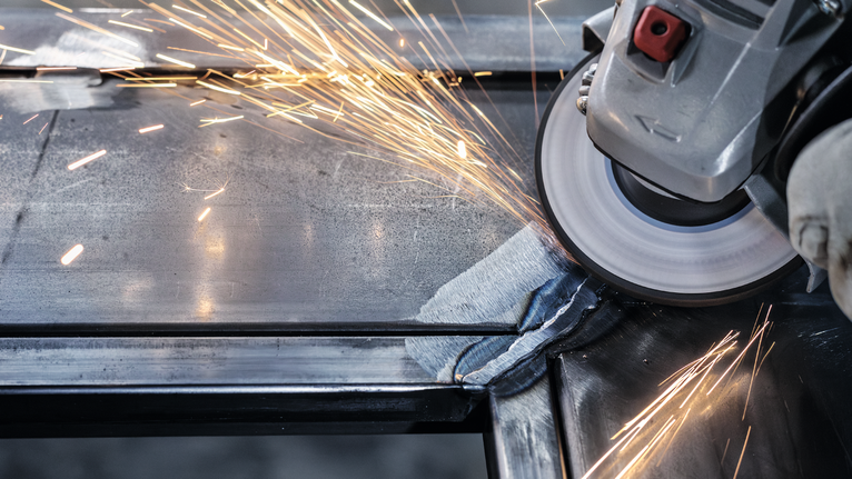 Orang yang mengenakan peralatan keselamatan menggiling logam, menghasilkan percikan terang.