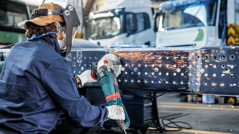 Orang yang mengenakan peralatan keselamatan menggiling balok logam, sehingga menimbulkan percikan api.