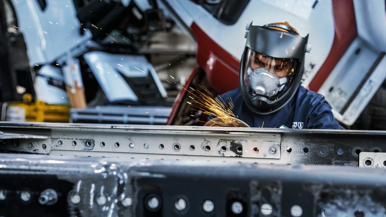 Orang yang mengenakan peralatan keselamatan menggiling logam, menghasilkan percikan terang.