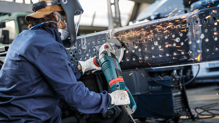 Orang yang mengenakan peralatan keselamatan menggiling sinar logam, sehingga menghasilkan percikan terang.