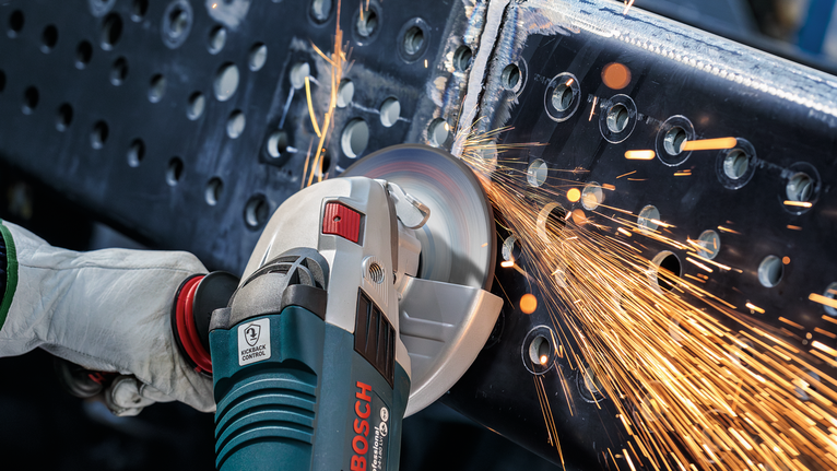 Orang yang mengenakan peralatan keselamatan menggiling balok logam, sehingga menimbulkan percikan api.