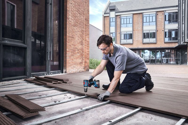 Seseorang yang mengenakan peralatan keselamatan memasang papan dek menggunakan bor tanpa kabel.