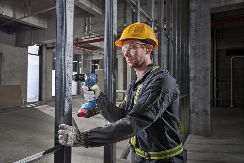 Seseorang yang mengenakan peralatan keselamatan mengebor rangka logam di lokasi konstruksi.