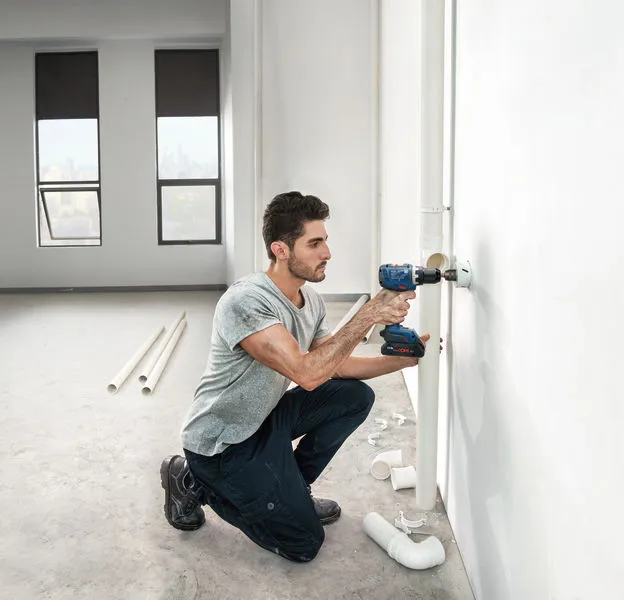 Seseorang mengebor dinding di samping pipa ledeng di ruangan yang setengah jadi.