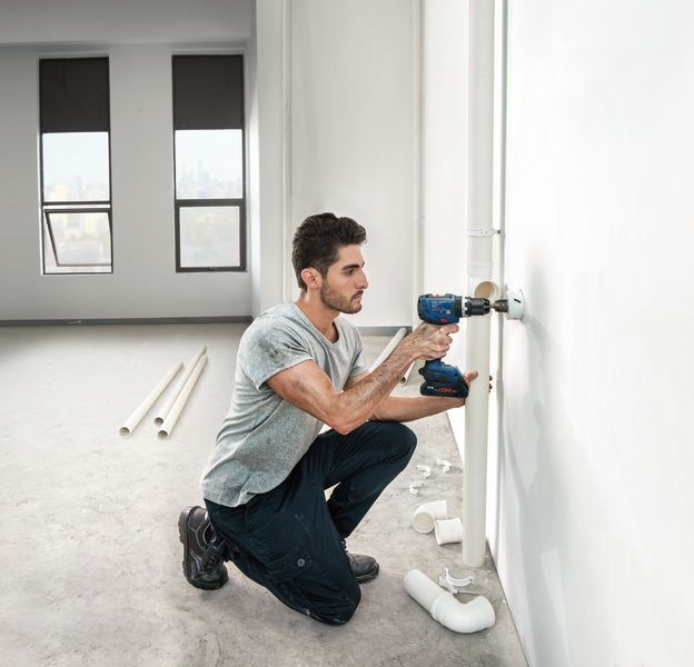 Seseorang mengebor dinding untuk memasang pipa di ruangan terang yang belum selesai.