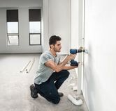 Seseorang mengebor dinding untuk memasang pipa di ruangan terang yang belum selesai.