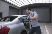 Orang yang mengenakan peralatan keselamatan menggunakan gergaji bolak-balik untuk memotong bingkai jendela belakang mobil.