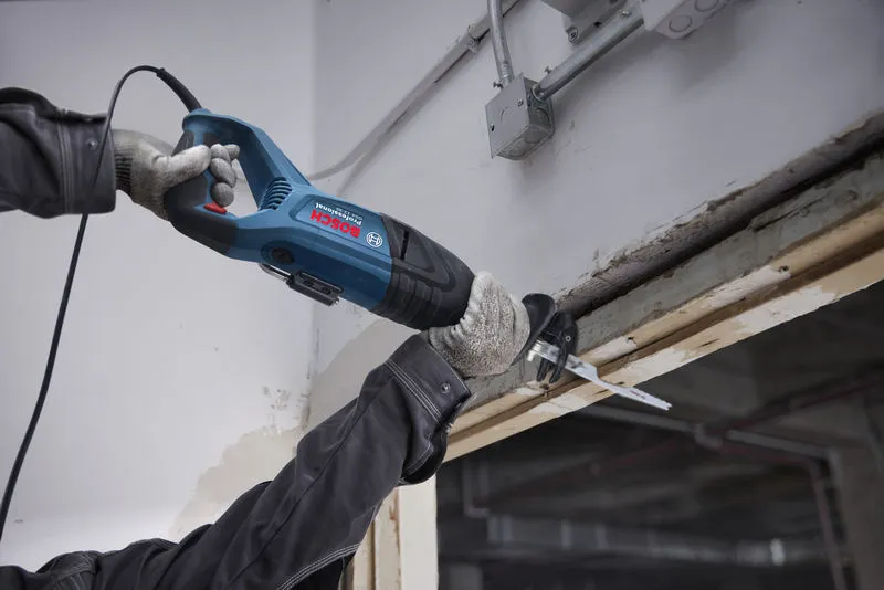 Seseorang yang mengenakan peralatan keselamatan mengoperasikan gergaji bolak-balik untuk memotong balok kayu.