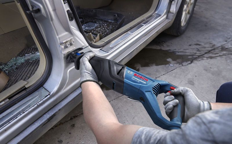 Seseorang yang mengenakan peralatan keselamatan menggunakan gergaji bolak-balik untuk memotong logam pada kusen pintu mobil.