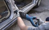 Seseorang yang mengenakan peralatan keselamatan menggunakan gergaji bolak-balik untuk memotong logam pada kusen pintu mobil.