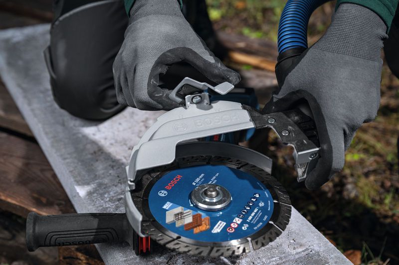 Seseorang yang mengenakan perlengkapan keselamatan memasang pelindung penyedot debu pada penggiling sudut besar.