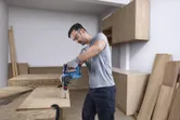Seseorang yang mengenakan peralatan keselamatan mengebor kayu menggunakan palu putar tanpa kabel.