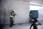 Seseorang yang mengenakan perlengkapan keselamatan menggunakan bor sementara alat perataan laser memproyeksikan garis merah.