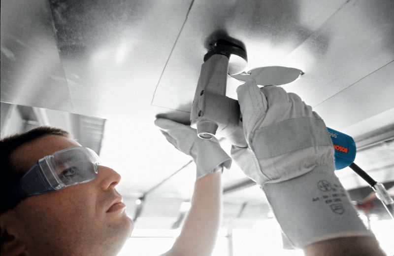 Seseorang yang mengenakan perlengkapan keselamatan menggunakan gunting untuk memotong lembaran logam.