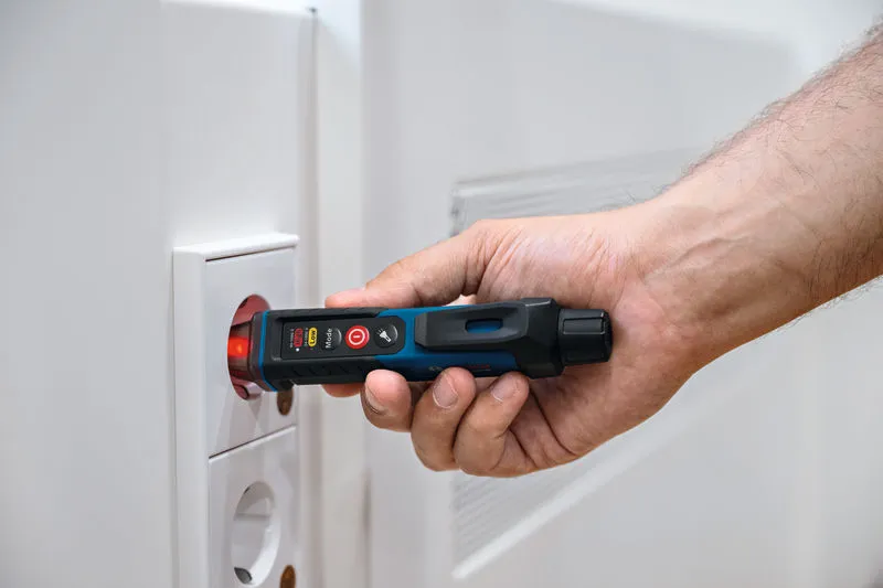 Seseorang menggunakan penguji tegangan non-kontak di dekat soket listrik.