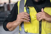 Orang yang mengenakan peralatan keselamatan menempatkan penguji tegangan non-kontak di saku rompi.