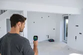 Seseorang memindai dinding putih dengan kamera termo di ruangan yang belum selesai.