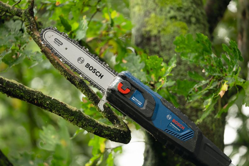 Pemangkas teleskopik tanpa kabel yang memotong cabang pohon di area luar ruangan yang rindang.